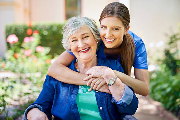 A smiling caregiver hugging a happy senior woman in a garden setting, showing warmth, trust, and supportive living care.