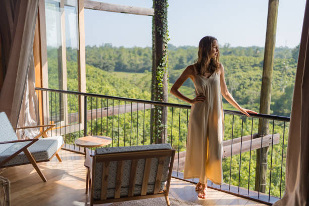Peaceful retreat scene with a woman admiring the green landscape from a balcony with cozy chairs and natural surroundings.